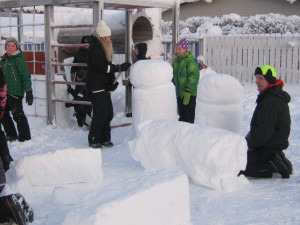En flicka som skulpterar i snö medan en pojke tittar på