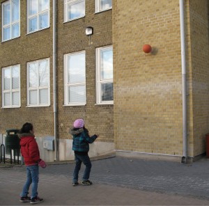 Två flickor som leker med en boll som de kastar på en skolvägg